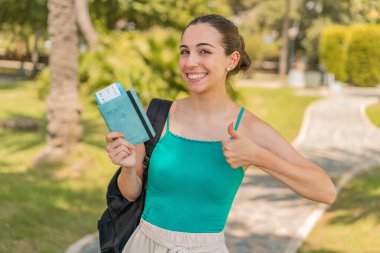 Dışarıda pasaportu olan genç ve güzel bir kadın. Başparmakları havada. Çünkü iyi bir şey oldu.