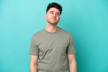 Kafkasyalı genç adam mavi arka planda izole edilmiş. Taraf ararken şüphe duyuyor.