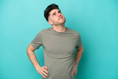 Genç beyaz adam mavi arka planda izole edildi. Çaba sarfettiği için sırt ağrısı çekiyor.