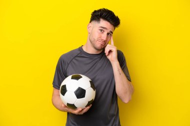 Yakışıklı genç futbolcu sarı arka planda izole edilmiş bir fikir düşünüyor.