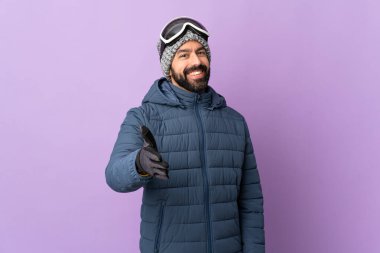 Snowboard gözlüklü kayakçı mor arka planda iyi bir anlaşma için el sıkışıyor.