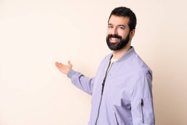 Sakallı, ceketli, soyutlanmış arka planda beyaz bir adam. Davet etmek için ellerini yana uzatıyor.