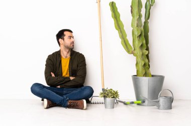 Bahçıvan içeride yerde oturuyor. Yan tarafa bakıyor.