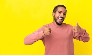 Sarı arka planda izole edilmiş genç latin adam baş parmak işareti yapıyor.