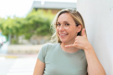 Dışarıda genç sarışın bir kadın. Gözlüklü ve telefon hareketleriyle.