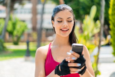 Açık havada genç ve güzel bir bayan cep telefonuyla mesaj ya da e-posta yolluyor.