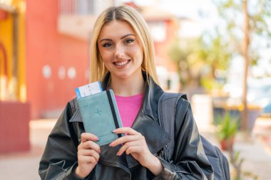 Sarışın, güzel bir kadın elinde pasaport tutarken gülümsüyor.