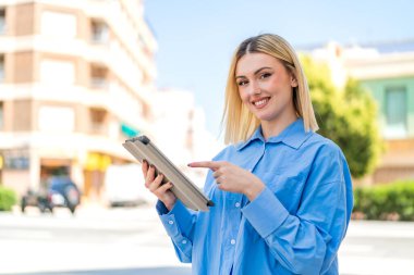Dışarıdaki güzel sarışın kadın tablet ekranına mutlu bir ifadeyle dokunuyor.
