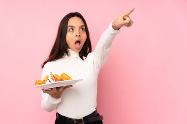 İzole edilmiş pembe arka planda waffle tutan genç esmer kadın