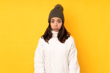 Kışlık şapkalı genç kadın izole edilmiş sarı arka planda üzgün ve depresif bir ifadeyle