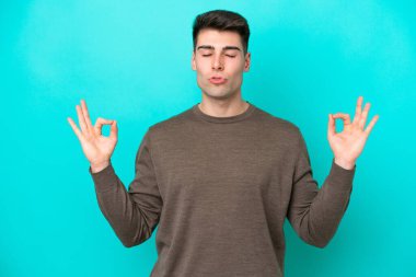 Zen pozisyonunda mavi arka planda izole edilmiş genç beyaz bir adam.