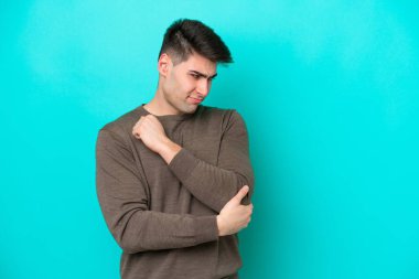 Genç beyaz adam mavi arka planda izole edilmiş, dirsek ağrısı var.