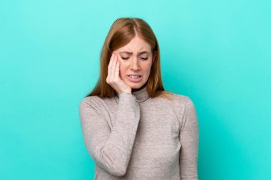 Mavi arka planda diş ağrısı olan genç kızıl saçlı kadın izole edilmiş.