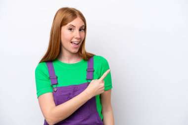 Beyaz arka planda izole edilmiş genç kızıl saçlı kadın şaşırmış ve işaret ediyor.