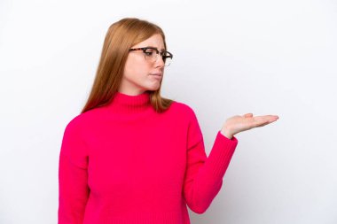 Genç kızıl saçlı kadın beyaz arka planda izole edilmiş. Kopyalama alanını şüphe ile tutuyor.