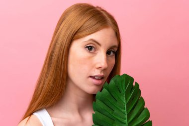 Pembe arka planda, elinde palmiye yaprağı olan genç, kızıl saçlı bir kadın. Portreyi kapat