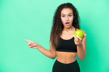 Yeşil arka planda izole edilmiş elmalı genç bir Arap kadın şaşırmış ve işaret ediyor.