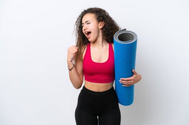 Genç Arap spor kadını yoga derslerine giderken beyaz arka planda izole edilmiş bir minder tutarak zaferi kutluyor.