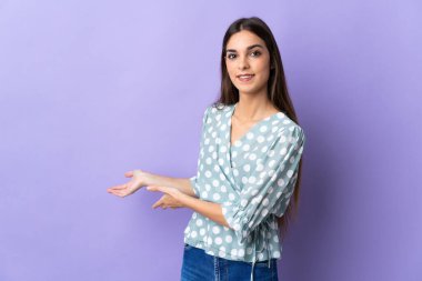 Mavi arka planda izole edilmiş genç beyaz kadın, davet edilmek için ellerini yana uzatıyor.