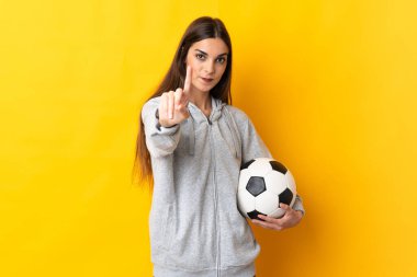 Sarı arka planda izole edilmiş genç futbolcu kadın parmağını kaldırıyor ve gösteriyor.