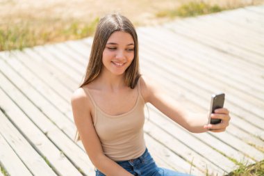 Dışarıdaki genç kız cep telefonuyla selfie çekiyor.