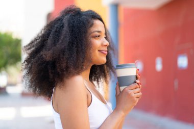 Genç Afrikalı Amerikalı kadın açık havada elinde kahve tutuyor.