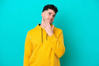 Genç beyaz adam mavi arka planda izole edilmiş gülümserken yukarı bakıyor.