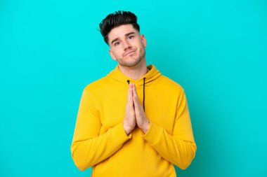Mavi arka planda izole edilmiş genç beyaz adam avuç içlerini bir arada tutuyor. İnsan bir şey ister.