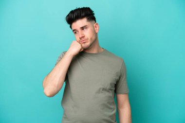 Kafkasyalı genç adam mavi arka planda izole edilmiş, yorgun ve sıkılmış bir ifadeyle