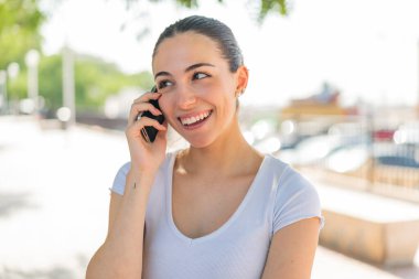 Açık havada genç ve güzel bir kadın cep telefonuyla sohbet ediyor.