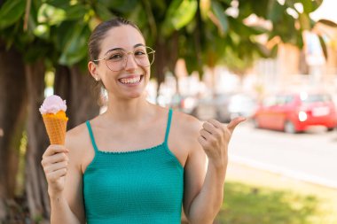 Açık havada kornet dondurması olan genç ve güzel bir kadın bir ürün sunmak için kenarı işaret ediyor.