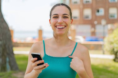 Dışarıda cep telefonu kullanan genç ve güzel bir kadın. Sürpriz bir yüz ifadesi var.