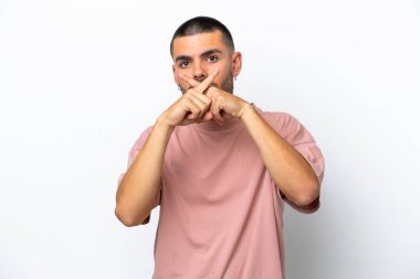 Beyaz arka planda izole edilmiş genç beyaz bir adam sessizlik işareti gösteriyor.