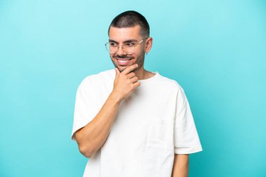 Kafkasyalı genç adam mavi arka planda izole edilmiş, yana bakıyor ve gülümsüyor.