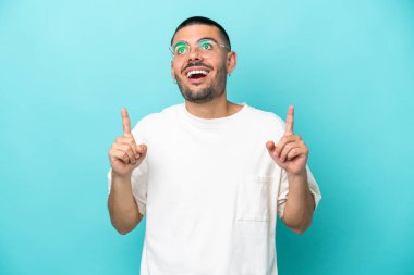 Mavi arka planda izole edilmiş genç beyaz adam şaşırmış ve yukarı bakıyor.