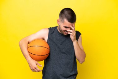 Beyaz tenli genç basketbolcu, sarı arka planda izole bir şekilde gülüyor.