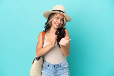 Pamel ve plaj çantalı genç Rus kız bir konferansta sunumdan sonra mavi arka planda izole bir şekilde alkışlıyor.