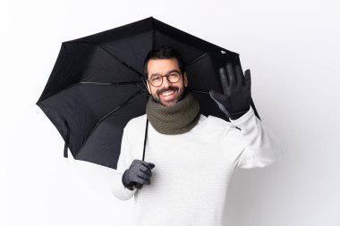 Beyaz saçlı, sakallı yakışıklı bir adam izole edilmiş beyaz duvarın üzerinde elinde şemsiyeyle mutlu bir ifadeyle selam veriyor.