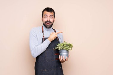 Arka planda bir bitkiyi tutan adam şaşırmış ve işaret ediyor.