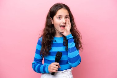 Küçük şarkıcı kız pembe arka planda izole edilmiş bir mikrofonu kaldırıyor ve ağzı açık bağırıyor.