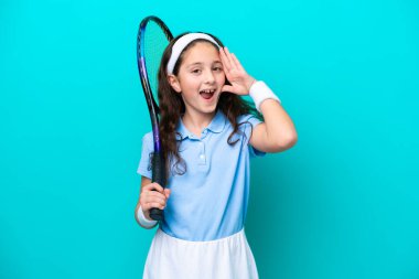 Tenis oynayan küçük beyaz kız mavi arka planda izole edilmiş, şaşırmış ve şok olmuş bir yüz ifadesi var.