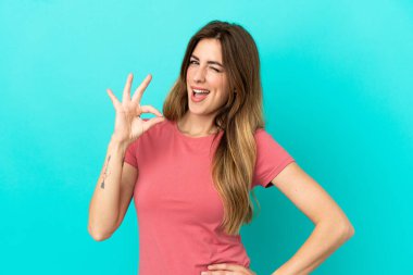 Mavi arka planda izole edilmiş beyaz bir kadın parmaklarıyla tamam işareti gösteriyor.