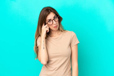 Kafkasyalı genç bir kadın mavi arka planda izole edilmiş bir fikir düşünüyor.