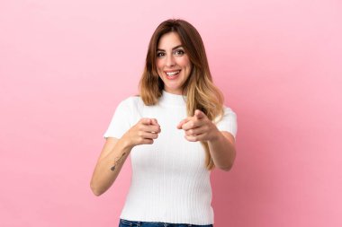 Pembe arka planda izole edilmiş beyaz kadın şaşırmış ve ön tarafı işaret ediyor.