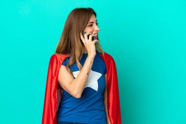 Süper kahraman beyaz kadın mavi arka planda izole edilmiş cep telefonuyla biriyle sohbet ediyor.