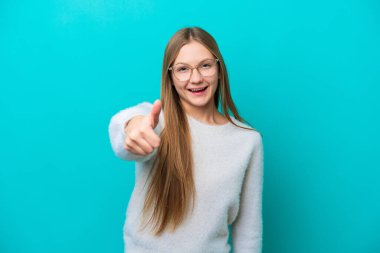 Genç Rus kadın mavi arka planda izole edildi. Başparmakları havada çünkü iyi bir şey oldu.
