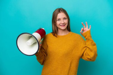 Mavi arka planda izole edilmiş genç bir Rus kadın elinde bir megafonla tamam işaretini parmaklarıyla gösteriyor.