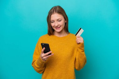 Genç Rus kadın mavi arka planda izole edilmiş cep telefonuyla kredi kartıyla alışveriş yapıyor.