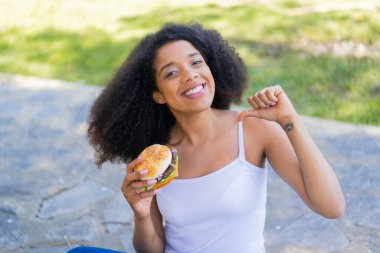 Genç Afrikalı Amerikalı kadın elinde burgerle gururlu ve kendini beğenmiş.