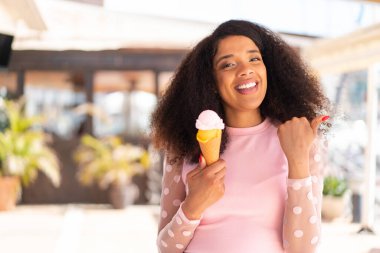 Açık havada kornet dondurması olan genç Afrikalı Amerikalı kadın bir ürünü sunmak için yan tarafı işaret ediyor.